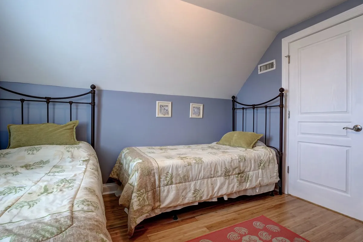 A cozy nook with two twin beds featuring floral bedding, surrounded by decorative framed art and warm wooden flooring. The setting is tranquil and inviting, perfect for sleepovers or quiet downtime for children.