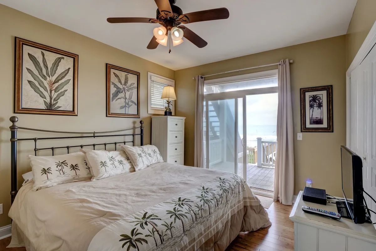 A tranquil master bedroom featuring a bed with a palm tree design, a window that allows in soothing natural light, and decorative wall art. The room exudes a sense of comfort and privacy, ideal for relaxation and recharging.