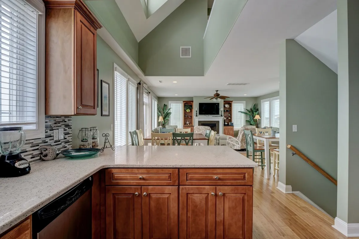 A wide-angle view of the open-concept living, dining, and kitchen area. The scene showcases a kitchen island, spacious dining table, and a comfortable living room setup, all bathed in natural light from large windows. The connection between spaces emphasizes togetherness, while the layout highlights seamless flow, ideal for group gatherings and family activities.