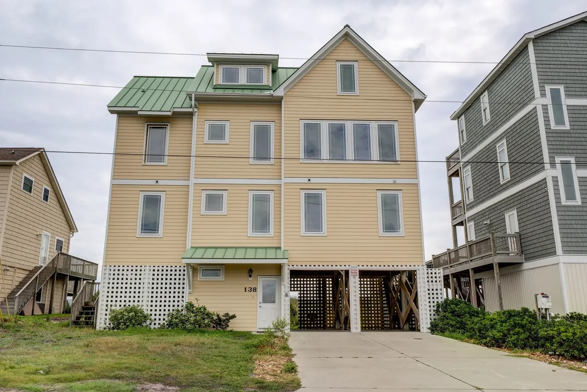 This image spotlights the house's unique architecture with a green roof, large windows, and an inviting porch area. The scene suggests a welcoming home base for returning after days spent exploring Surf City's eateries, shops, and local attractions. The porch invites evening gatherings and offers a vantage point to survey the surrounding area.