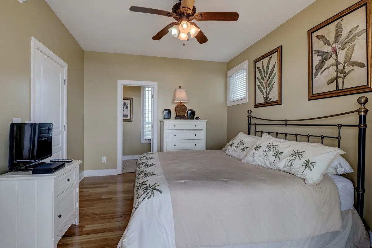A serene bedroom with a comfortable bed, nightstand and lamp, decorative wall art, and a television mounted for easy viewing from bed. The space is styled for relaxation and private moments of entertainment.