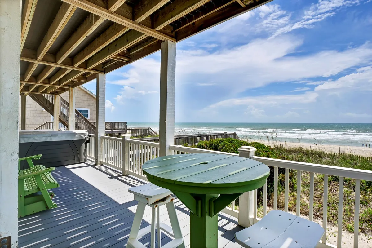 This image features a green outdoor table set on a deck with a clear view of the ocean. The white railing frames the space, inviting guests to dine or relax outdoors while enjoying the sea breeze and panoramic views. The deck area is ideal for group gatherings, morning coffee, or sunset dinners, tying the property directly to the coastal environment and the activities described in the section.