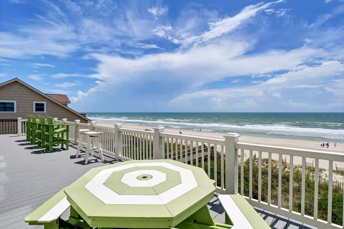 This image captures a beachfront view with green patio furniture arranged to face the ocean waves. The relaxed setting encourages outdoor dining, sunbathing, and casual socializing, aligning with the coastal and leisure-focused attractions mentioned in the section. The image evokes the atmosphere of a beach getaway where local cuisine and relaxation are central.